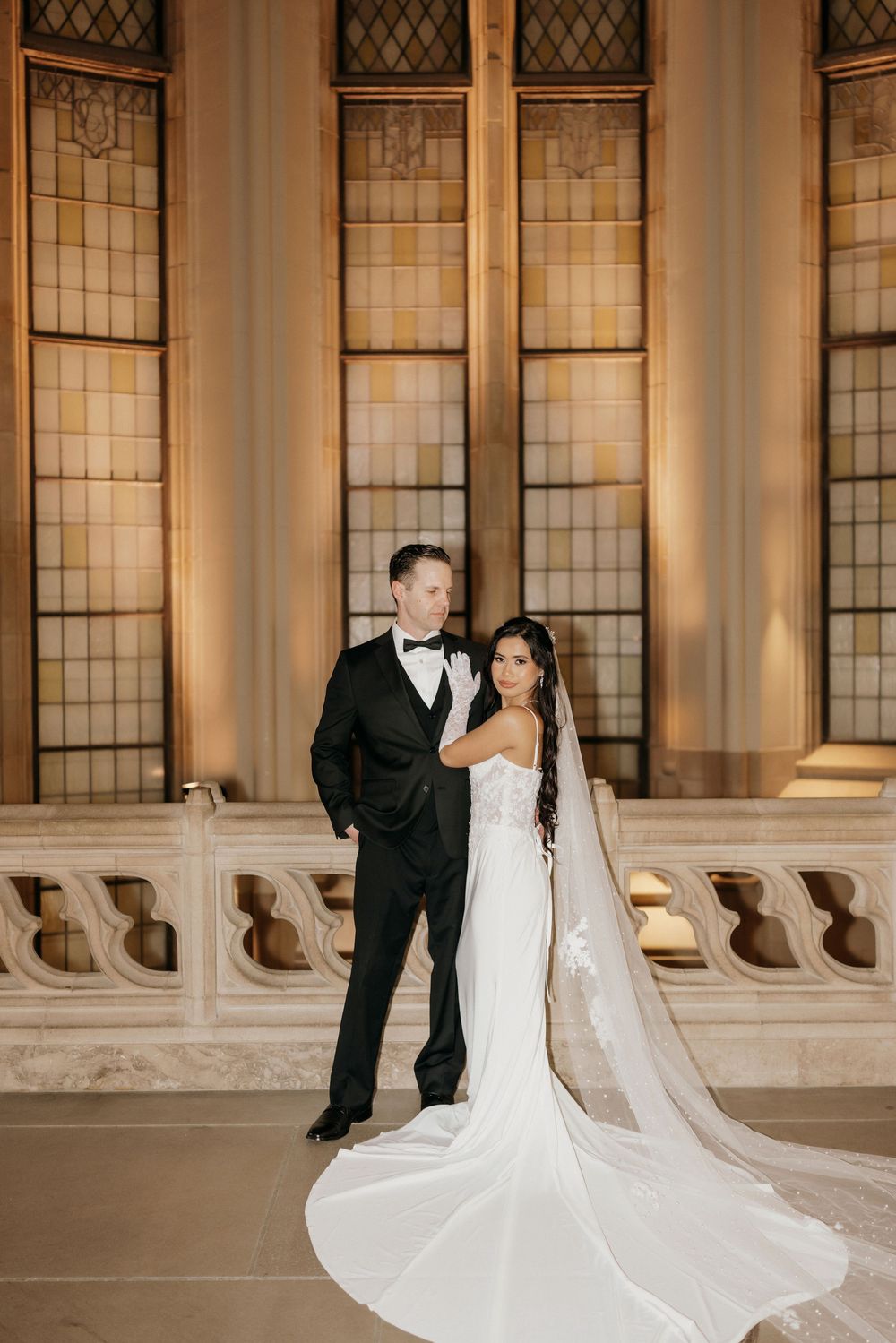 Newlyweds share an intimate moment in front of ornate Gothic windows with the bride's long train flowing behind.