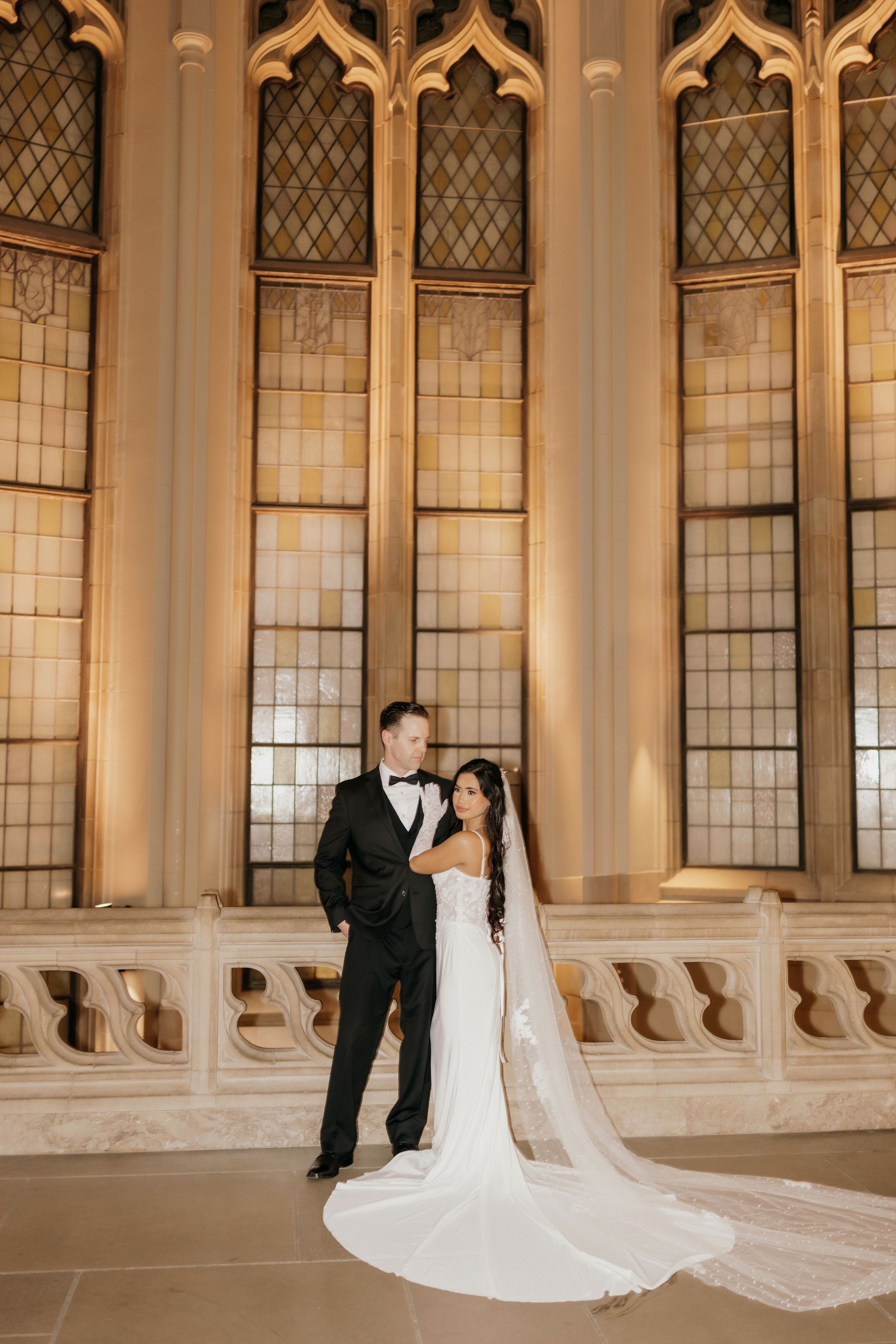 Wedding couple photographed against beautiful cathedral windows in a historic architectural setting.