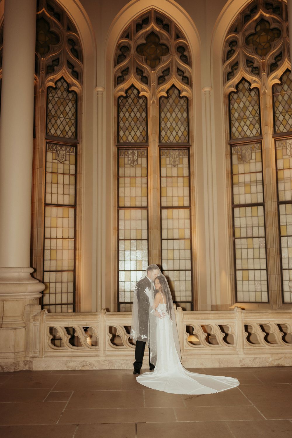 Elegant Gothic-style church interior with arched windows and stone columns creates a dramatic backdrop for bridal portraits.