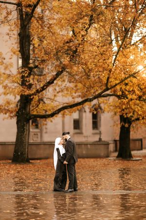 A couple shares a romantic moment under golden autumn trees with fallen leaves scattered on the ground.