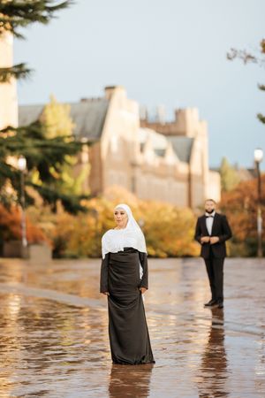 Creative wedding photo showing people standing in reflective water during golden hour with city buildings in background.