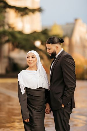 A couple in traditional Islamic dress poses together during golden hour by the water.