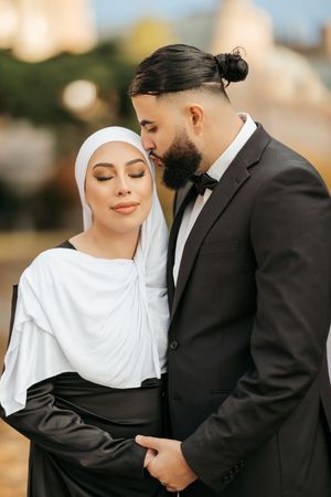A romantic wedding photoshoot series showing a couple in traditional white hijab and black suit embracing outdoors.