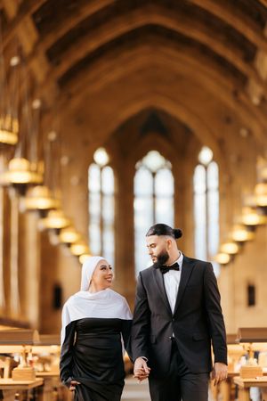 A couple walks through an elegant church dining hall with arched ceilings and warm lighting.