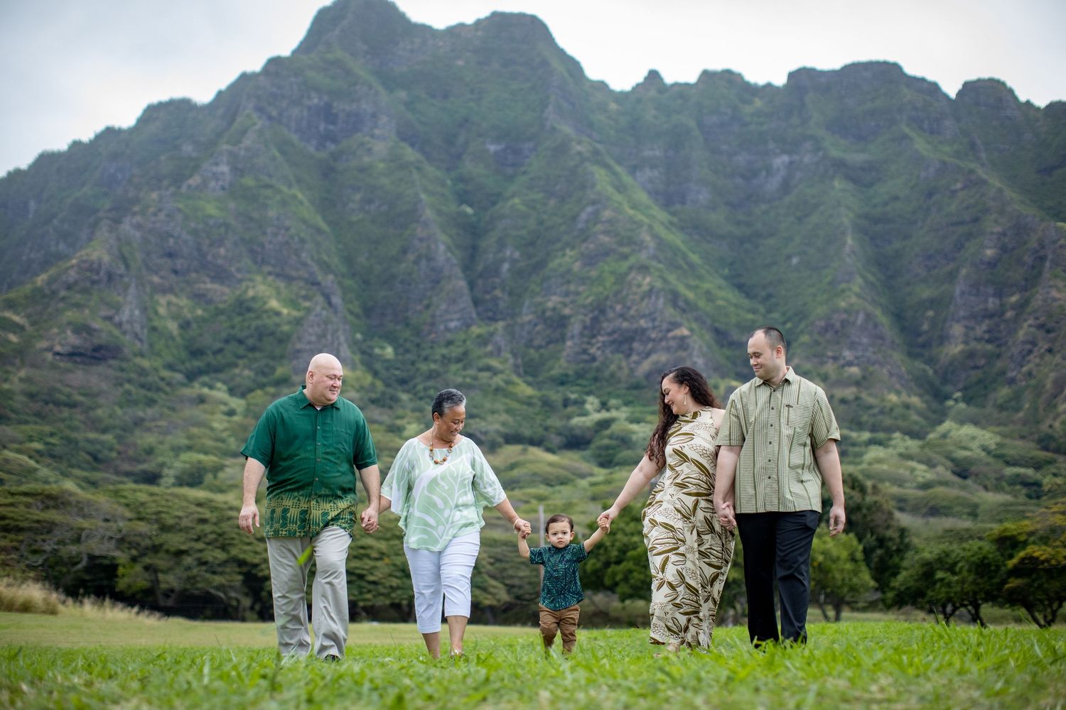 Family walking together on grassy field with majestic Ko'olau mountains rising dramatically in background.