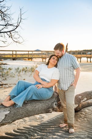 Romantic beach engagement photos with couple lounging on driftwood at sunset.