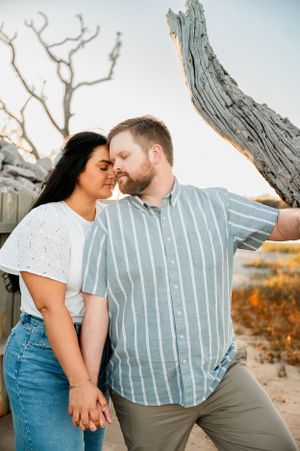 Casual engagement photos of couple in denim and stripes sharing intimate moments by weathered tree.