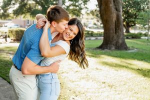 Playful couple laughing and embracing in sunny outdoor park setting.