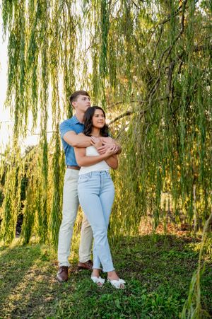 A romantic photoshoot under weeping willow trees with a couple in casual attire.