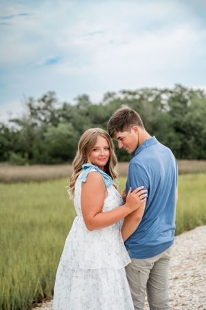 A couple shares tender moments along a marsh pathway on a sunny day.