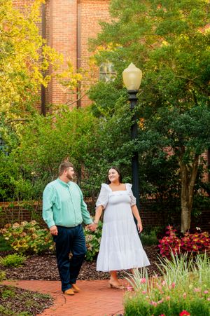 A couple walking through a garden with brick walls and autumn foliage.