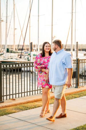 A waterfront engagement session with a couple walking along a marina boardwalk.