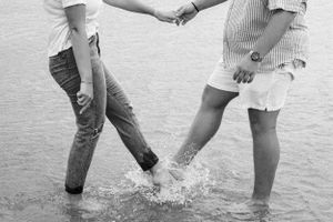 Two people splash and play in shallow water at the beach during a photoshoot.