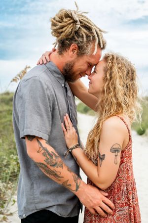 A romantic beach photoshoot featuring a couple in casual attire sharing intimate moments.