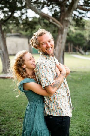 A playful couple laughing and embracing in a grassy outdoor setting.
