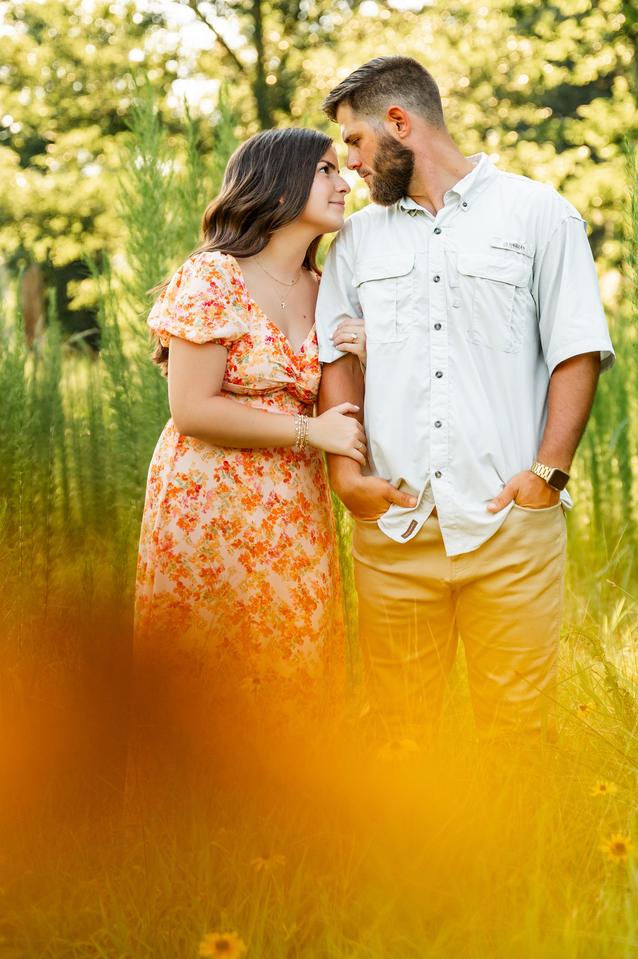 Romantic couple poses in golden sunlight with orange wildflowers in foreground.