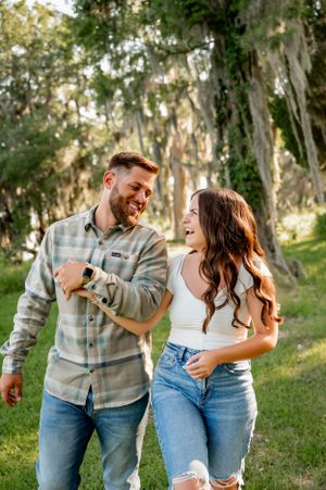 Playful couple laughing together in a wooded outdoor setting wearing casual denim and plaid.