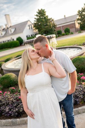 Couple sharing a romantic kiss in front of a fountain at an elegant estate during golden hour.