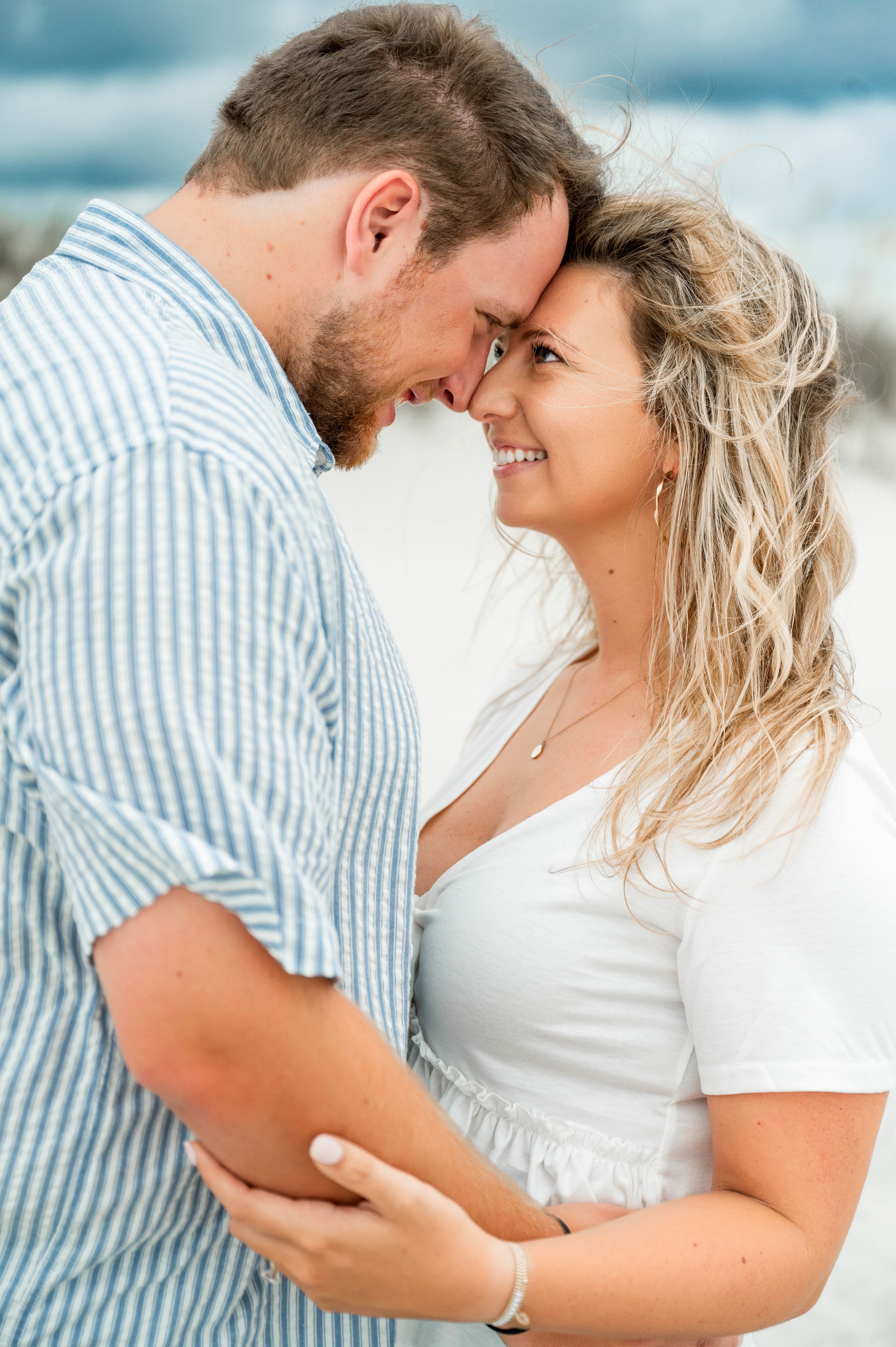 A couple embraces on a beach with soft lighting and ocean waves in the background.