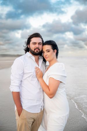 A romantic beach photoshoot at sunset with cloudy skies and ocean waves in the background.