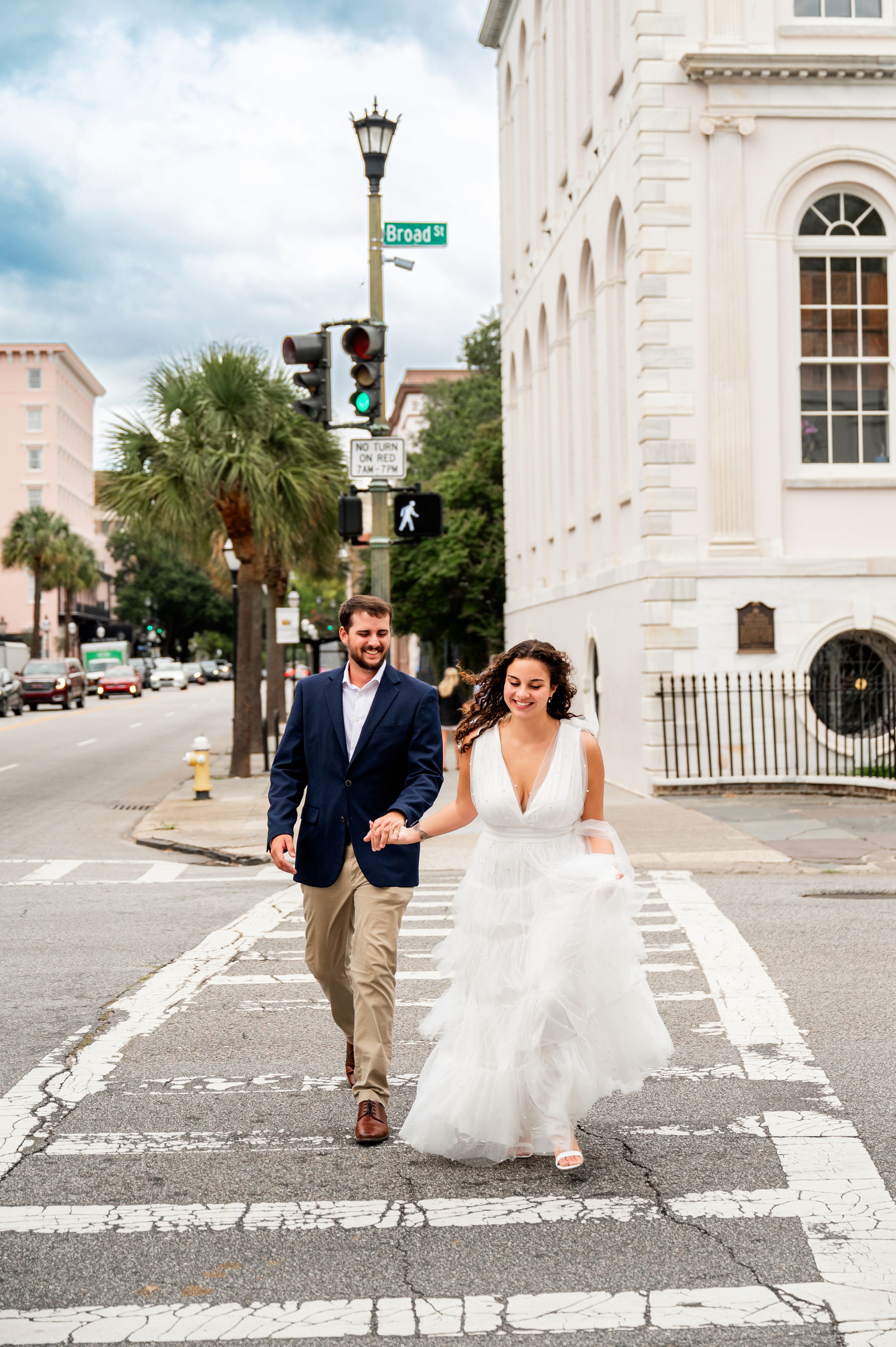 Newlyweds walking and laughing together on a historic Charleston street with white buildings.