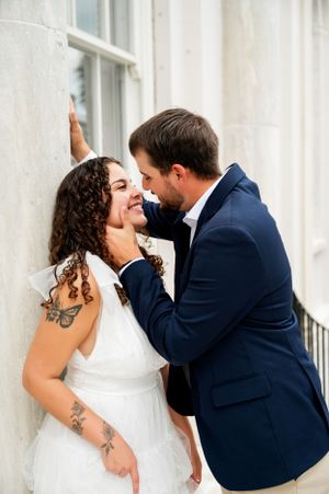 Wedding couple in navy and white sharing romantic kisses against a white building exterior.