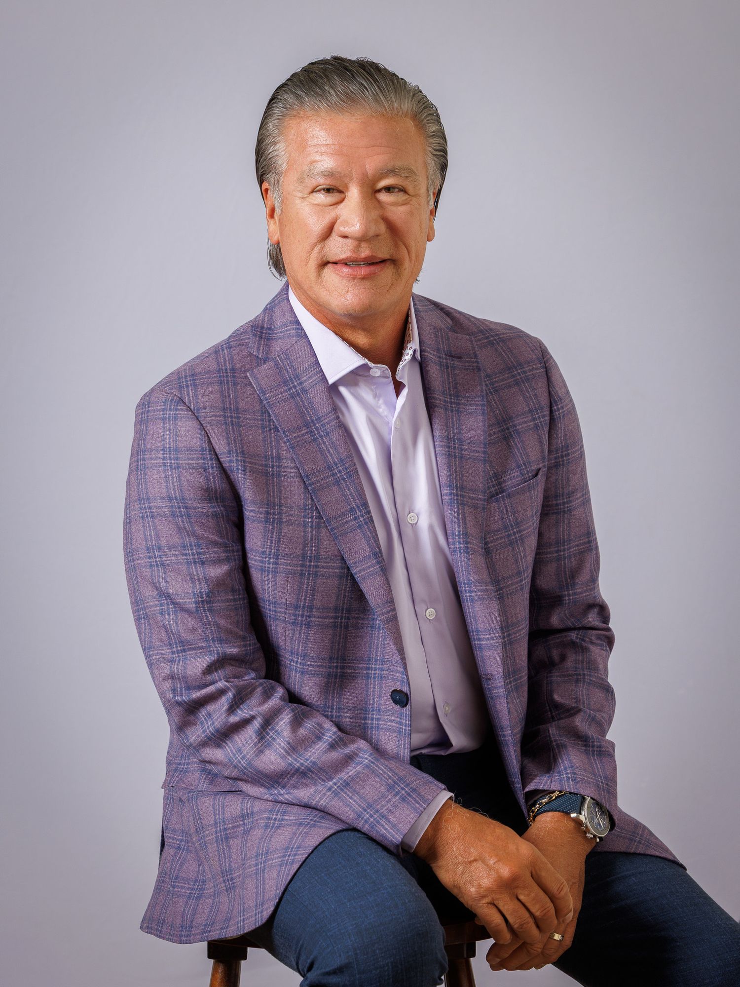 A person in a plaid blazer and white shirt poses for a series of professional headshots and seated portraits.