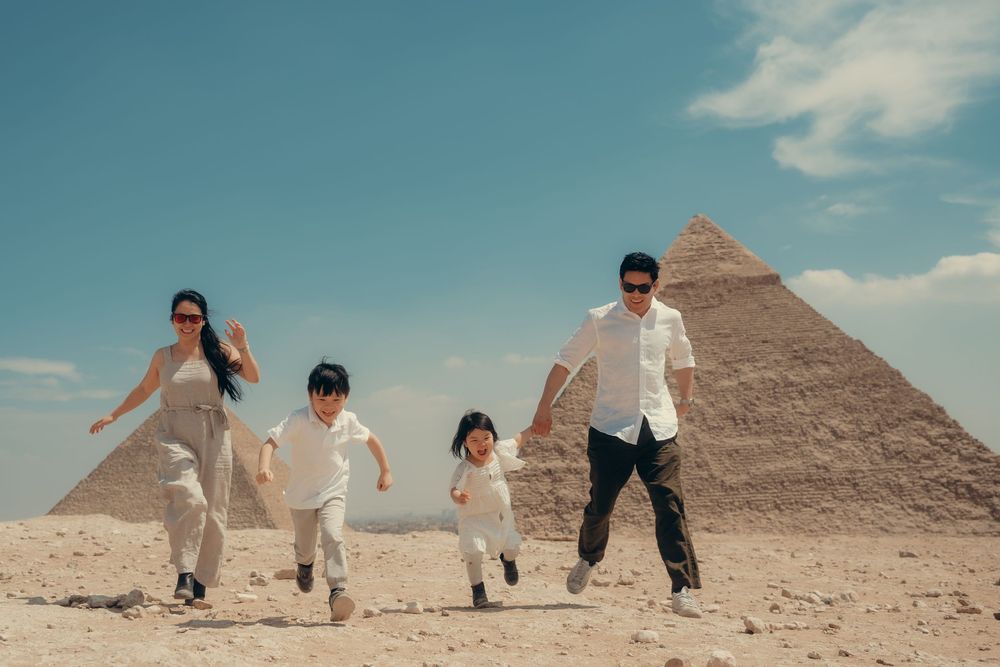 A sequence of people jumping in front of the ancient Egyptian pyramids in the desert under a bright blue sky.