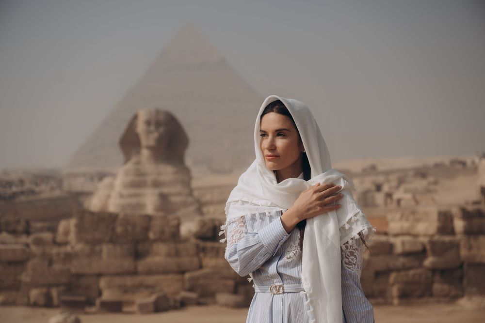 A woman in white clothing poses in front of the ancient Egyptian pyramids and Sphinx at Giza.