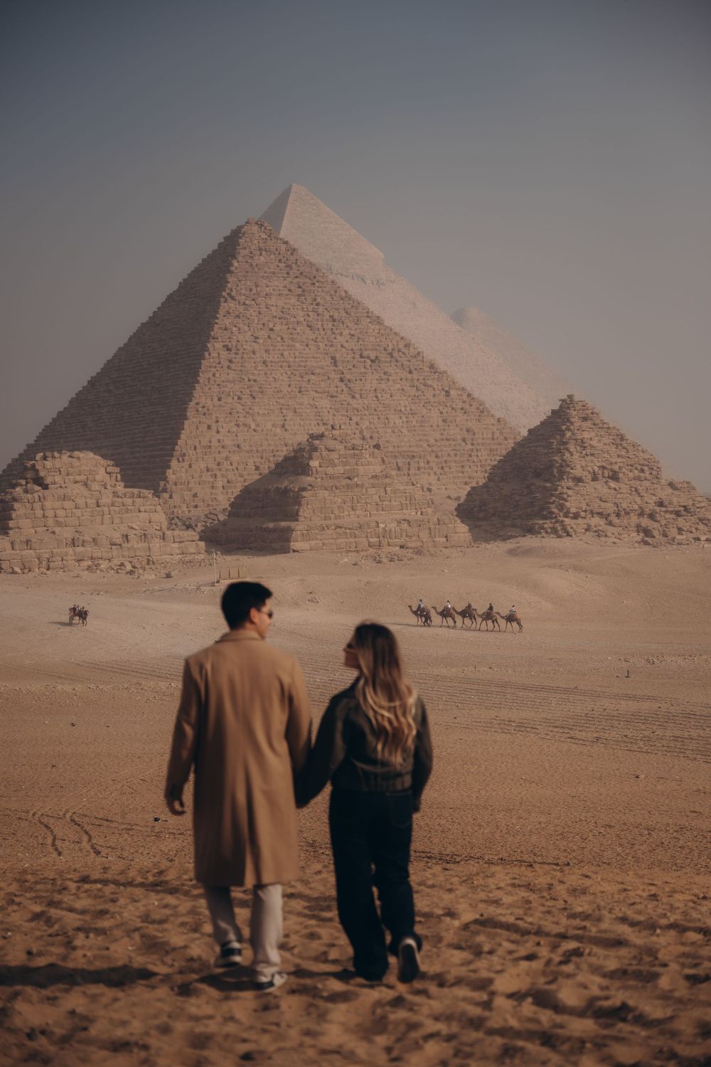 A couple admires the ancient pyramids of Giza while camels trek across the desert landscape in Egypt.