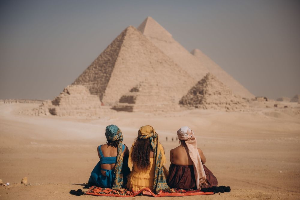 Tourists sit together overlooking the ancient pyramids of Giza in the Egyptian desert during sunset.