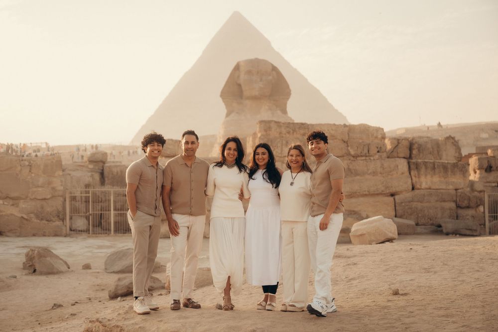 A group of tourists pose in front of the Great Sphinx and pyramids in Giza, Egypt at sunset.