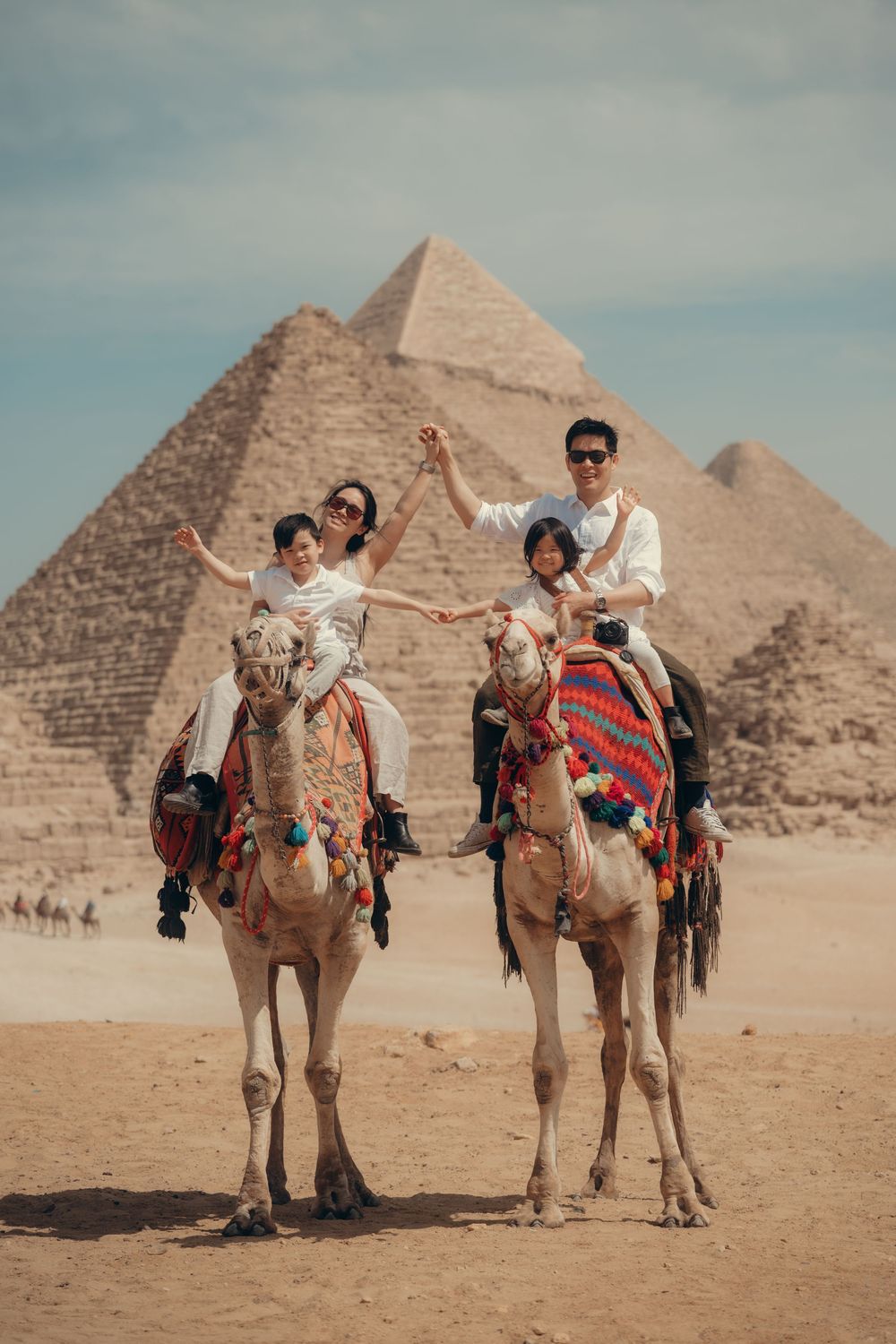 Tourists riding camels in front of the ancient pyramids of Giza in Egypt on a sunny desert day.