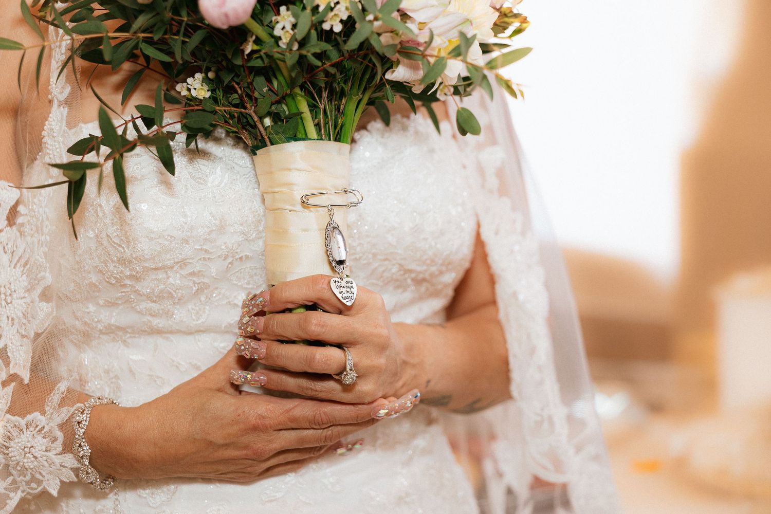 Close-up view of hands delicately holding a blush pink and white floral wedding bouquet with lush greenery.