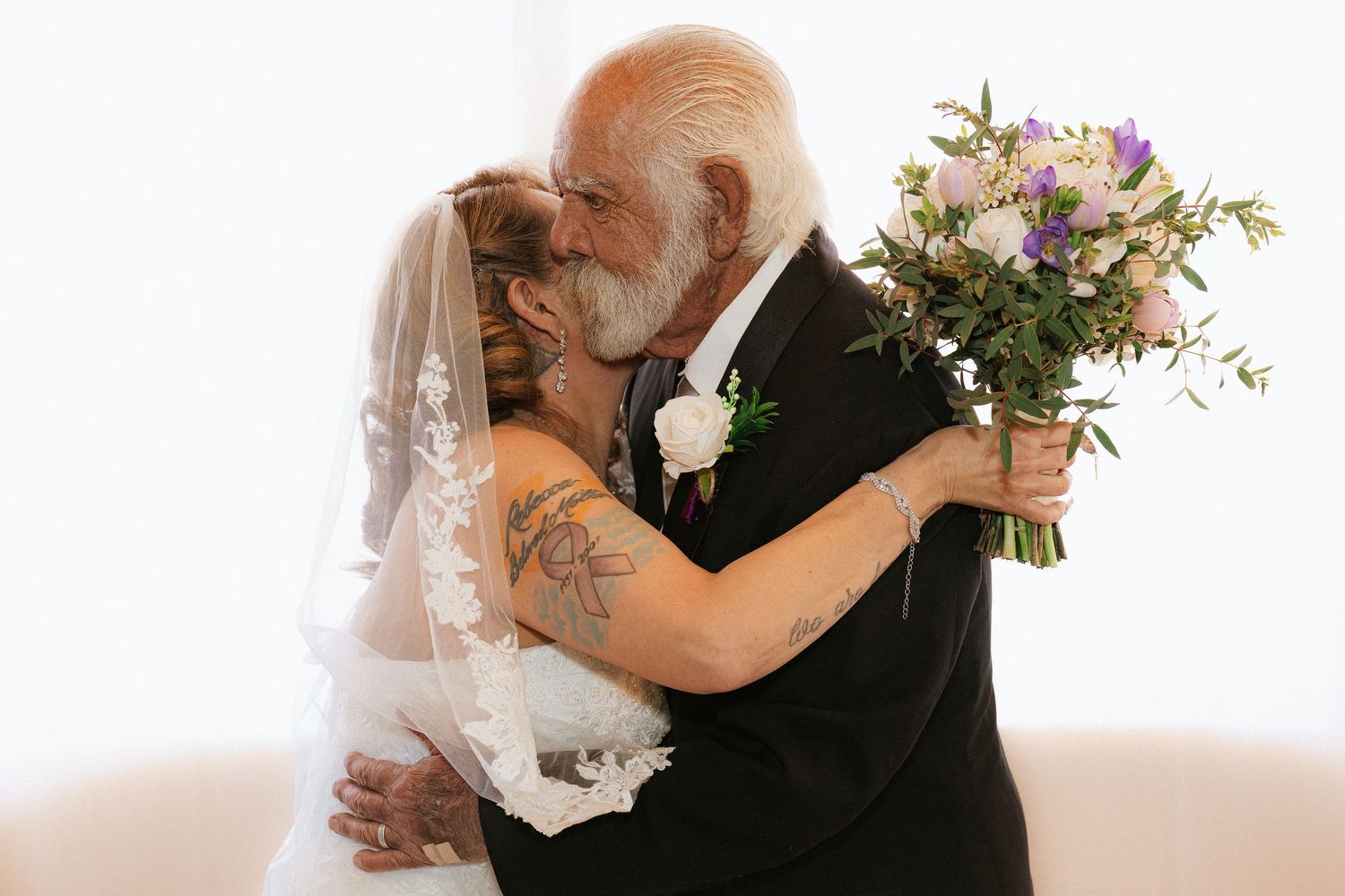 A bride and groom share an intimate embrace during their wedding celebration with the bride holding a floral bouquet.