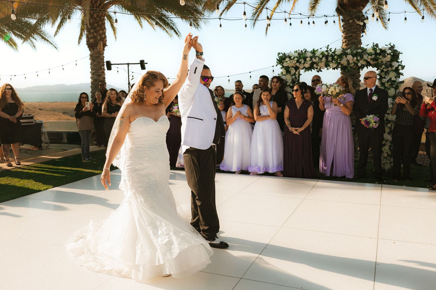 Wedding guests strike a fun celebratory pose in front of an ocean view during a beach ceremony at sunset.