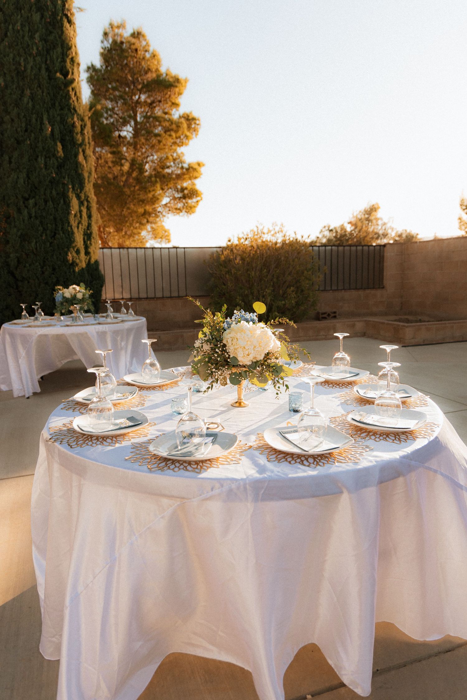 Elegant wedding reception tables with white linens and floral centerpieces set against a golden sunset backdrop.