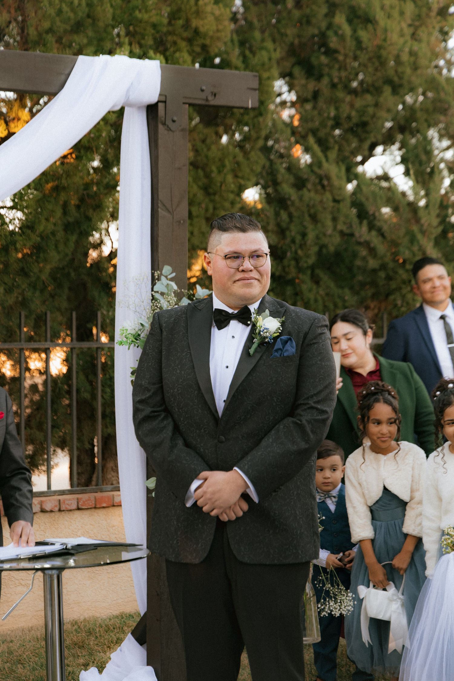 A wedding ceremony setup with a wooden arch decorated with white fabric outdoors during golden hour.