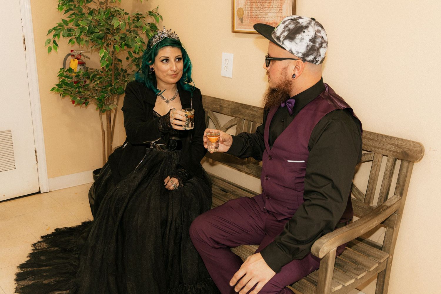 Two people sit on a wooden bench wearing traditional Middle Eastern clothing in an indoor setting.