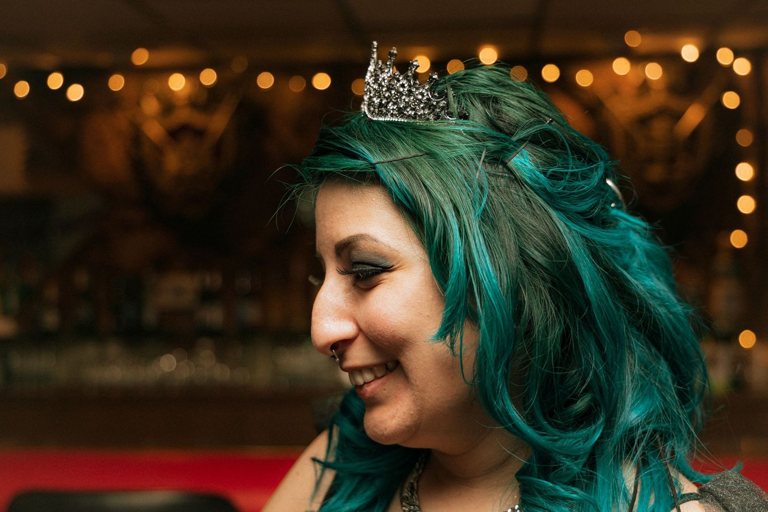 A bride with vibrant teal hair wears a sparkly crown and smiles during a romantic evening celebration.