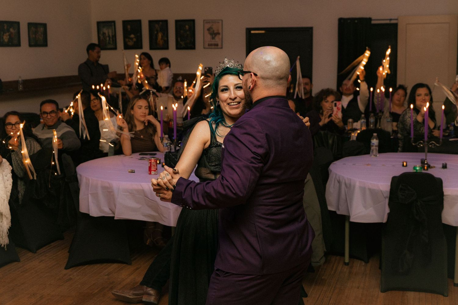Two dancers perform as others holding sparklers create an enchanting scene at a reception with round tables.