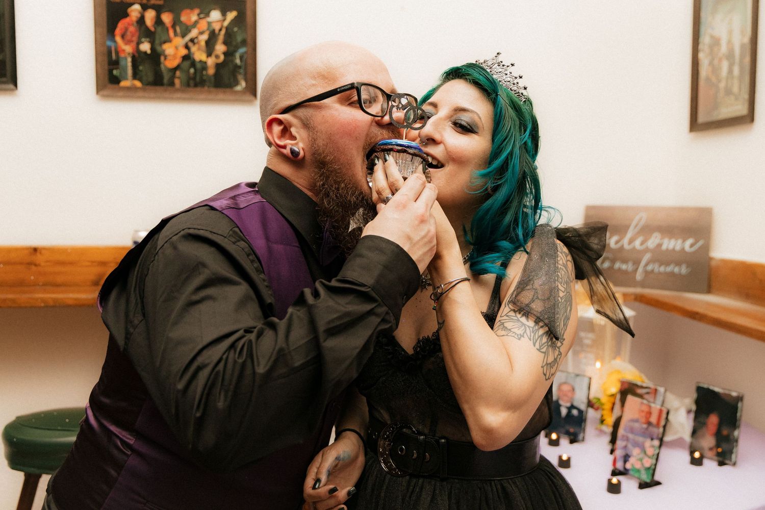 Couple in wedding attire share an intimate kiss in front of framed artwork at their wedding reception.