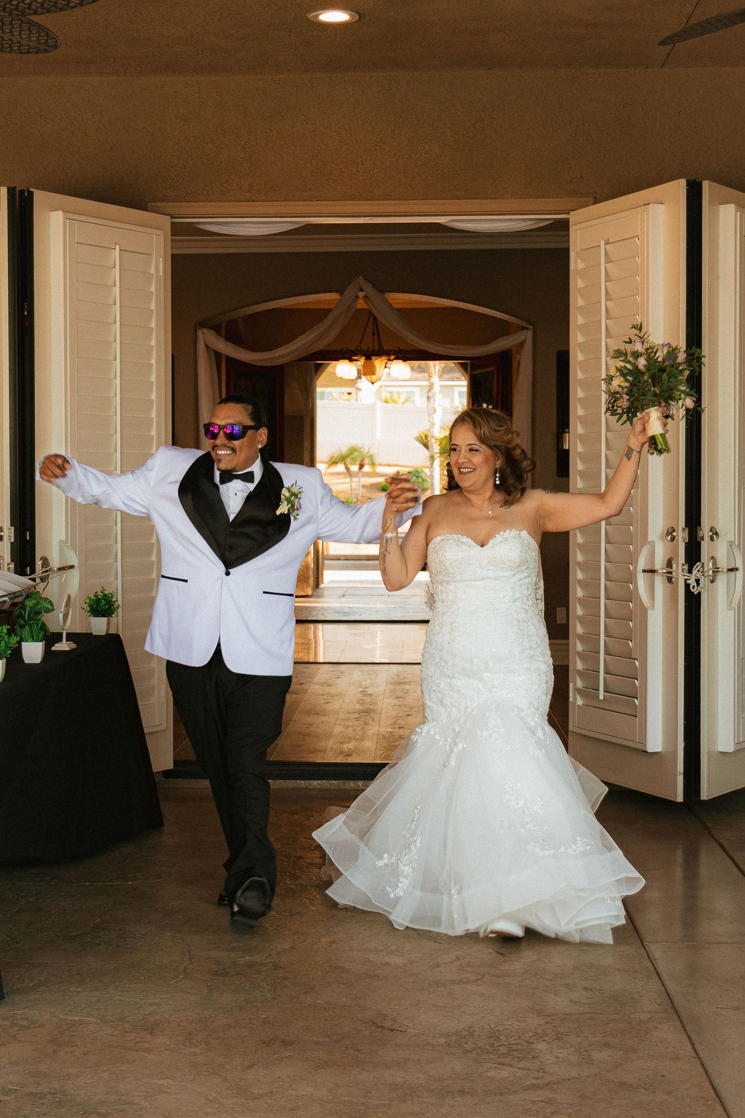 Two wedding guests make their entrance at a reception venue with dramatic poses and joyful expressions.