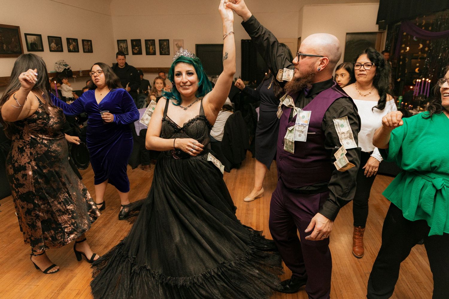 Dancers twirl on a wooden dance floor at an event, with spectators watching in the background.