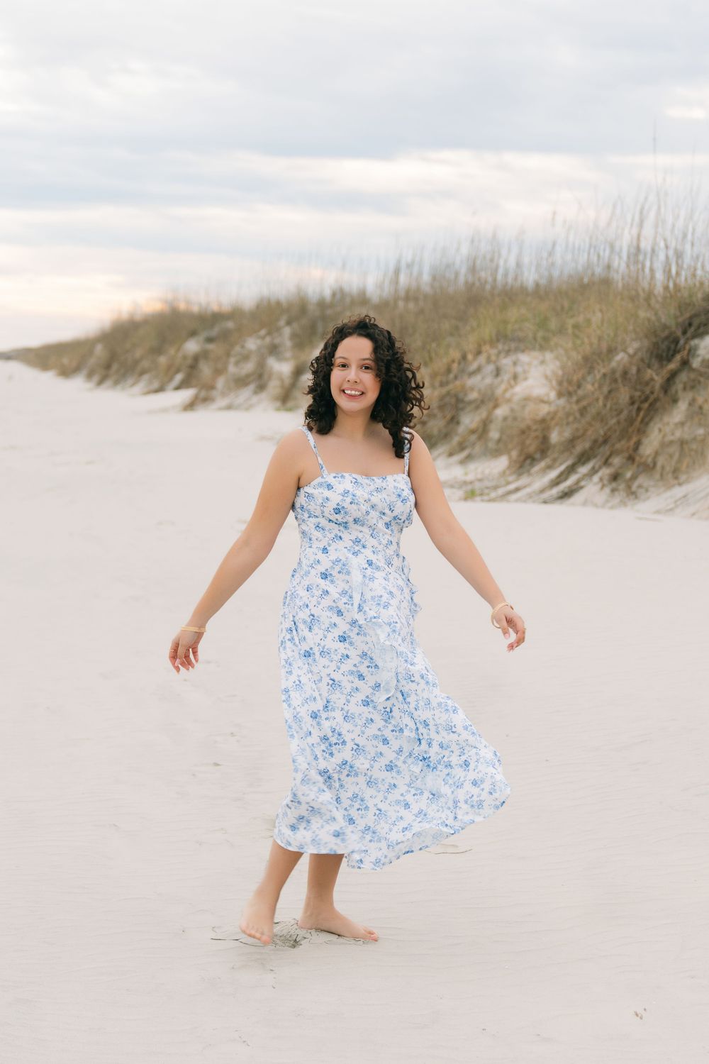 High school senior portraits at Corsair Beach on Jekyll Island, with Maria walking along the shore in a blue floral dress