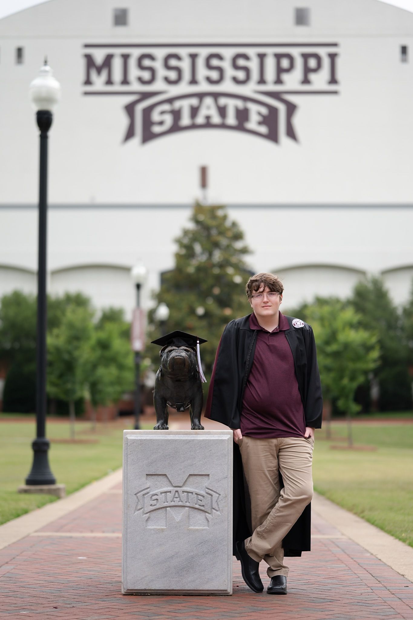 A person and a black dog pose in front of Mississippi State University building on campus.