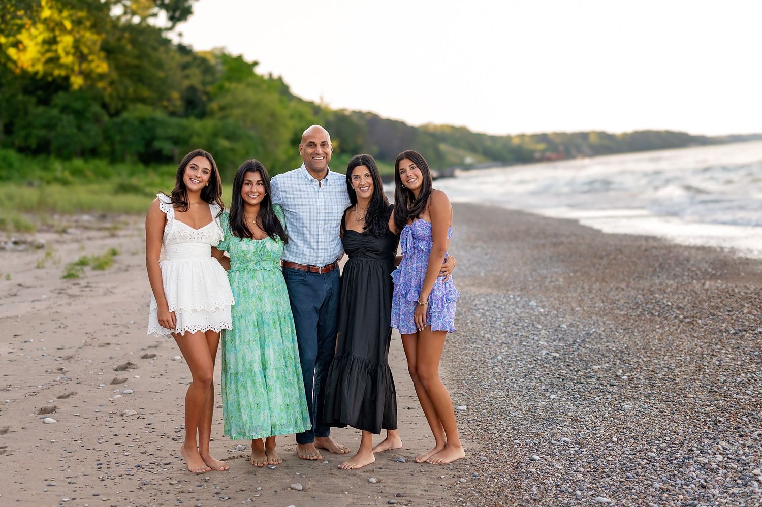Group of five people in summer dresses pose together on beach at sunset.