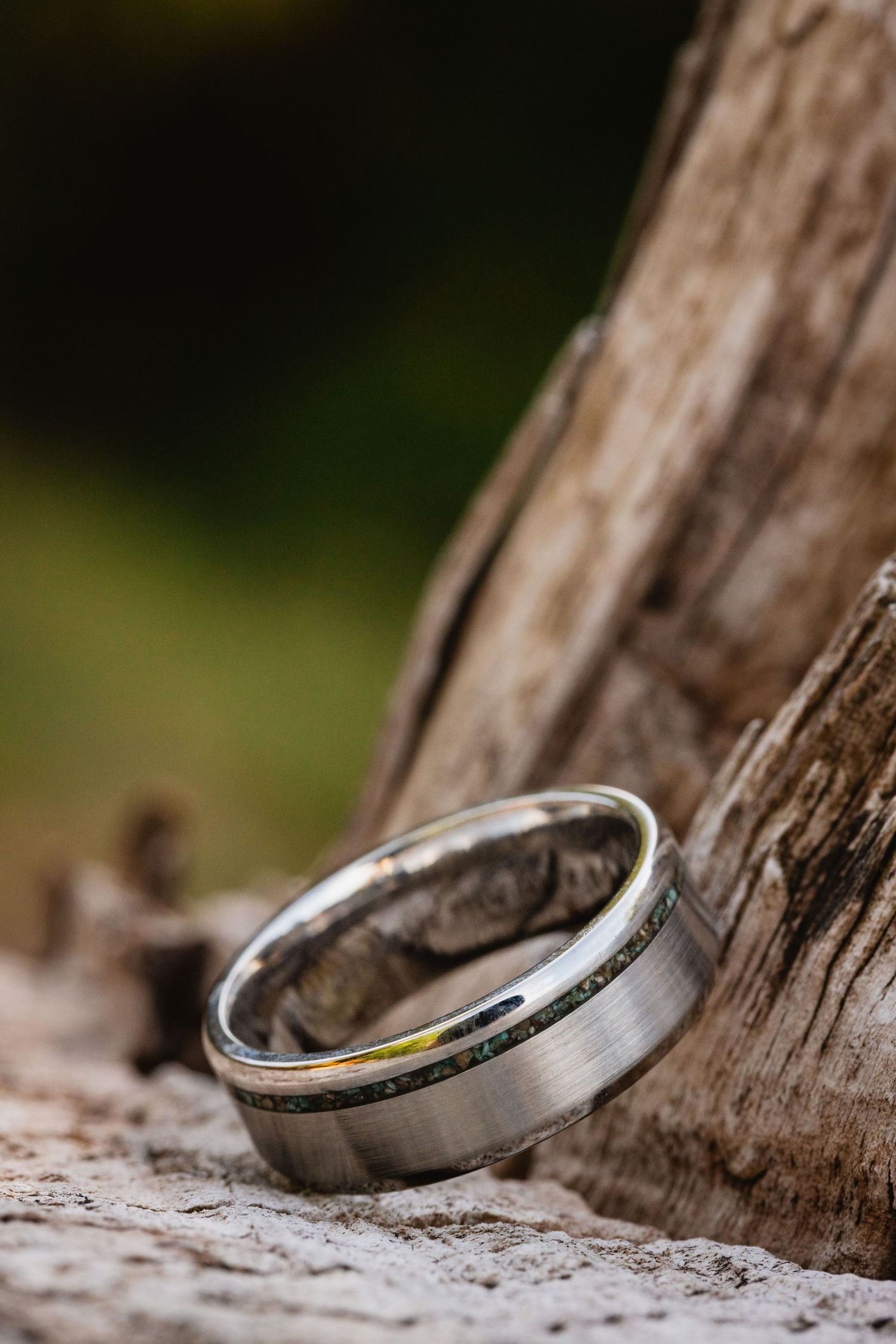 Close-up of bride and groom holding hands showing wedding ring with red rock desert landscape in the background.