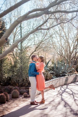 Couple sharing romantic moment under winter trees in garden pathway.