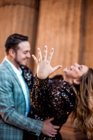 Couple celebrates engagement with woman showing ring in sparkling dress.